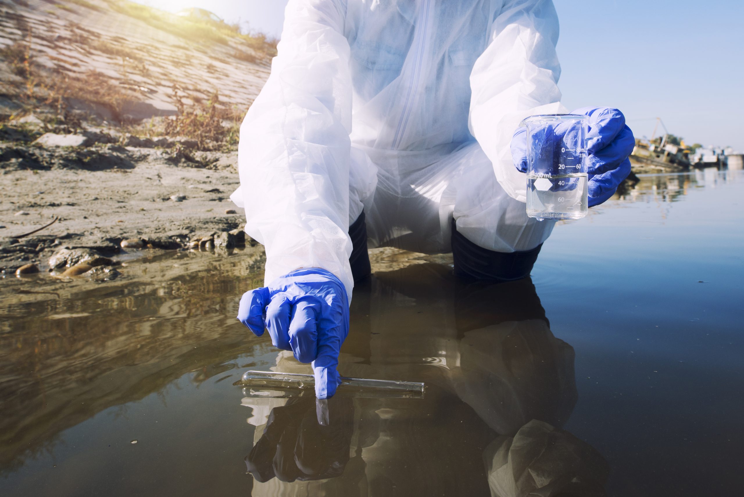 Unrecognizable ecologist taking samples of water with test tube from city river to determine level of contamination and pollution.