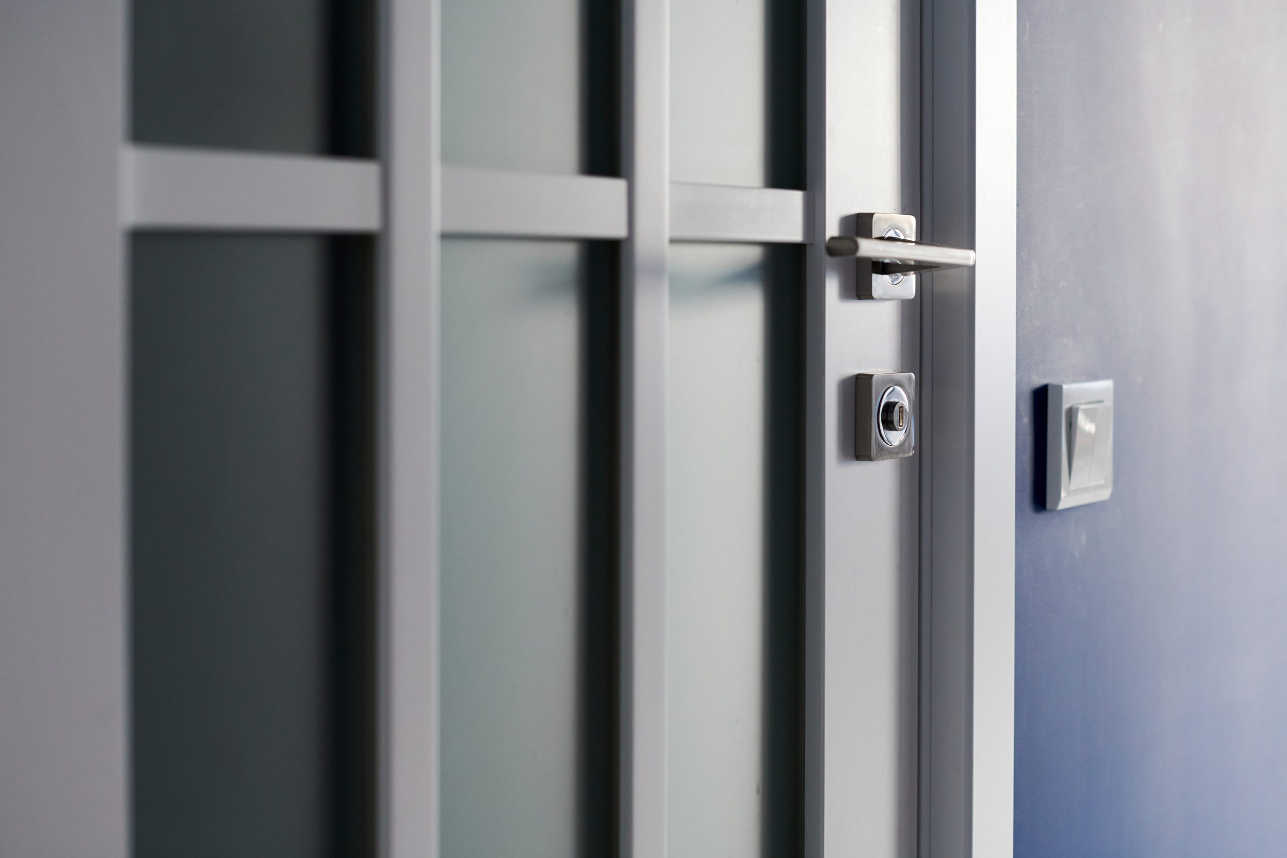 White interior door with handle. Blue wall in modern apartment, light switch nearby. Wooden closed door between rooms. Stylish hallway design